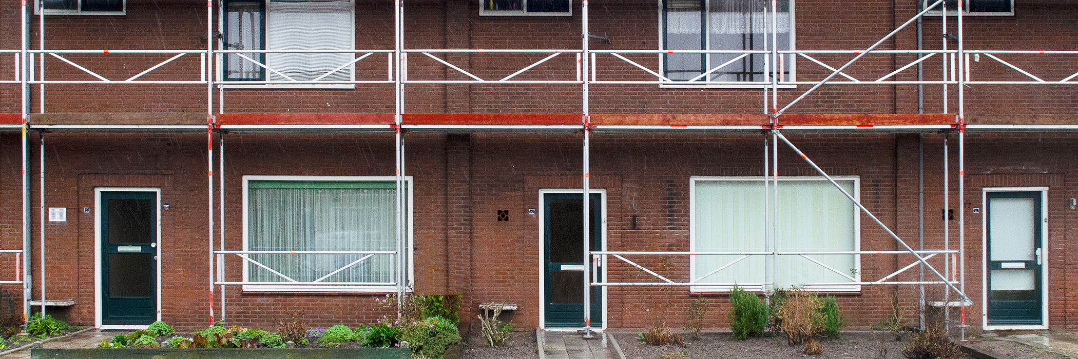 Woningen met donker bruin/rode bakstenen gevel, witte kozijnen, groene deuren met een steiger voor de deur