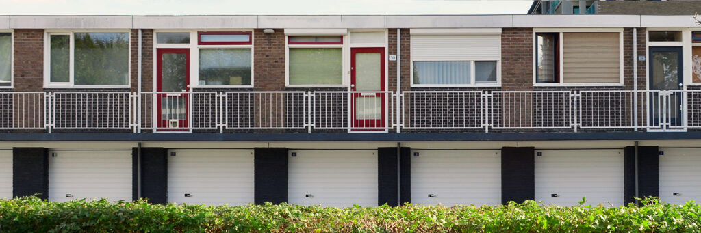Appartementen met bruine bakstenen gevel, witte kozijnen, rode deuren, garages op de onderste verdieping met bosjes ervoor