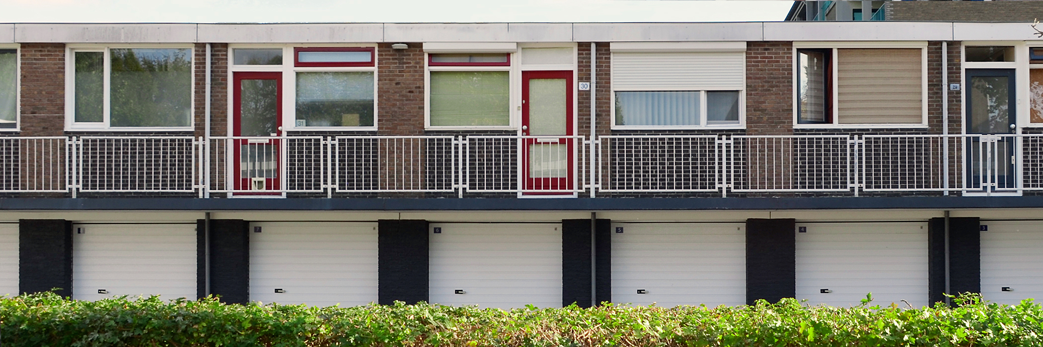 Appartementen met bruine bakstenen gevel, witte kozijnen, rode deuren, garages op de onderste verdieping met bosjes ervoor