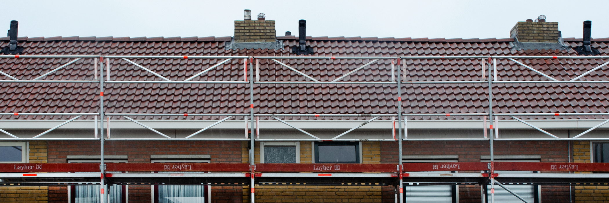 Woningen met bruine bakstenen gevel, witte kozijnen, rode dakpannen met een steiger ervoor van Layher