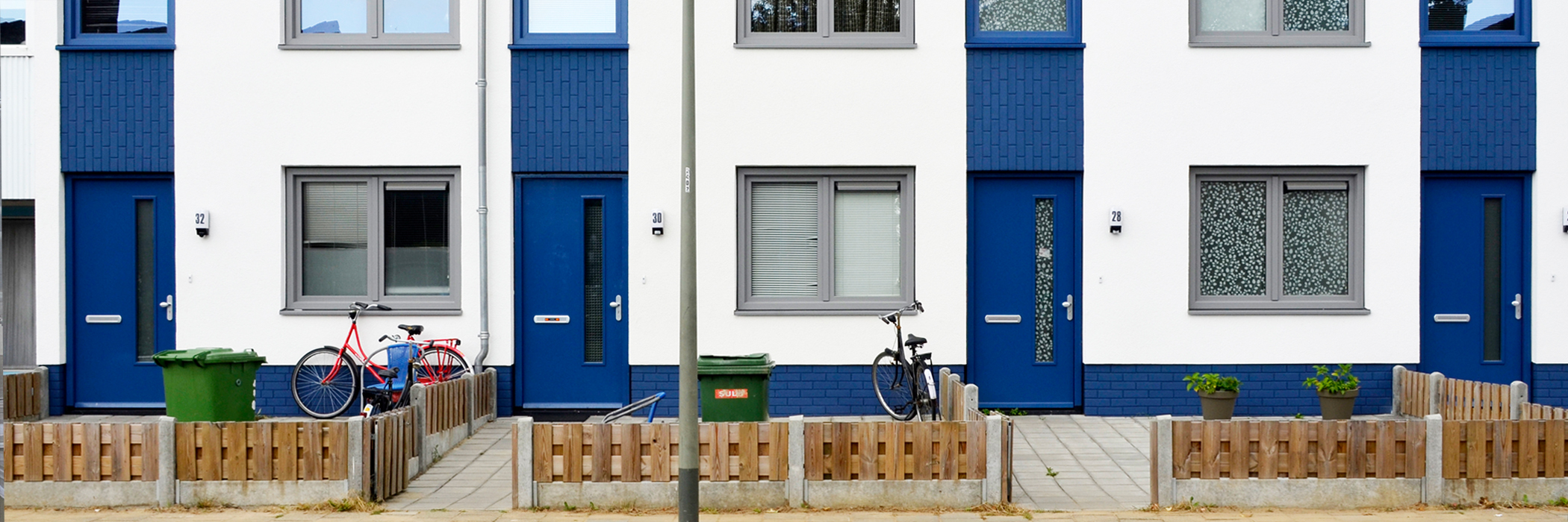 Woningen met witte gevel, blauwe deuren, grijze kozijnen, fietsen voor de deur, met een houten hekje en een lantarenpaal