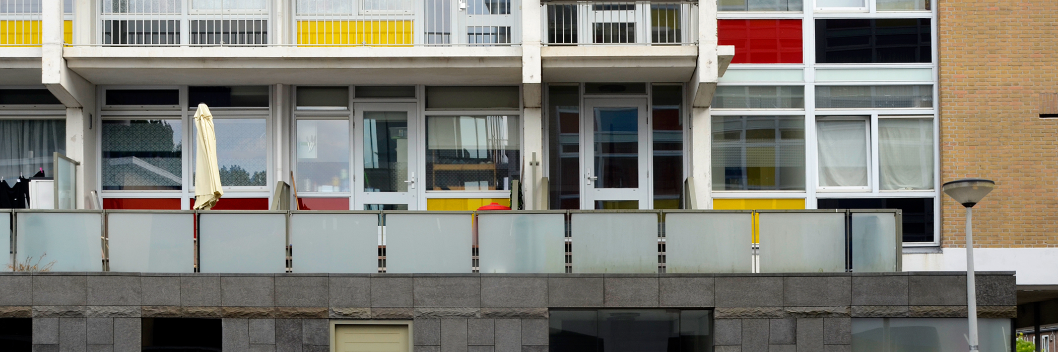 Appartementen met bruine bakstenen gevel, witte kozijnen en rood, wit en zwarte kunststof platen onder de ramen