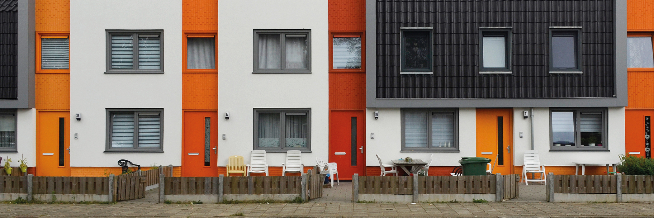 Woningen met witte gevel, oranje deuren, grijze kozijnen, zwarte dakpannen met een houten hekje voor de deur