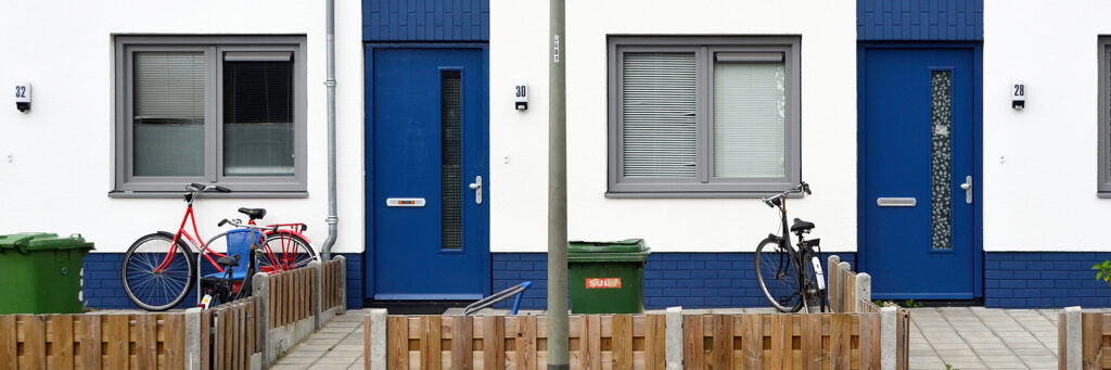 Woningen met witte gevel, blauwe deuren, grijze kozijnen, fietsen voor de deur, met een houten hekje en een lantarenpaal