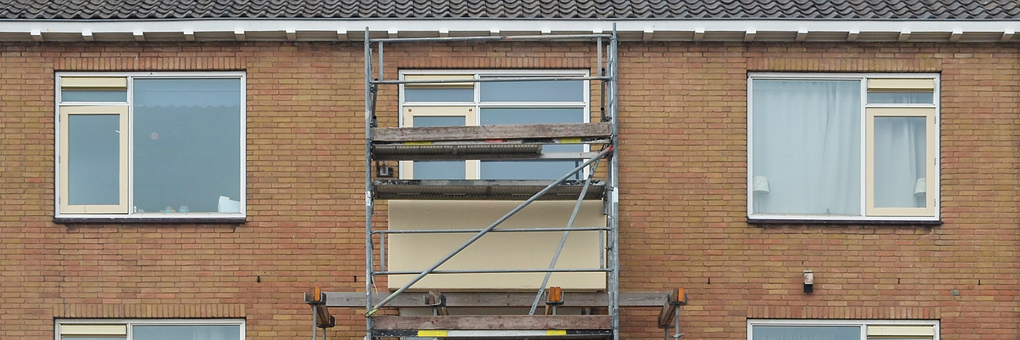 Woningen met licht bruine bakstenen gevel, witte kozijnen met gele ramen en een steiger voor de deur