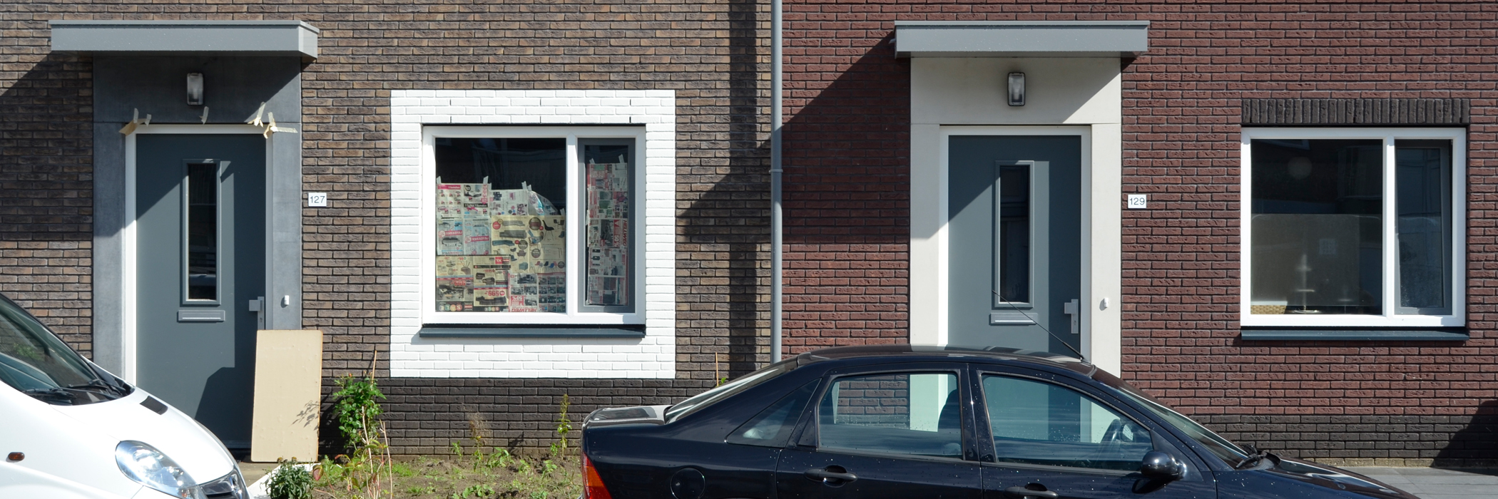 Woningen van bakstenen, de linker woning heeft een grijze rand om de voordeur, de rechter woning heeft een witte rand.