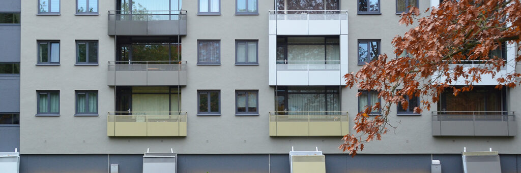 Appartementen met een grijze gevel, donker blauwe kozijnen en balkons in verschillende kleuren.