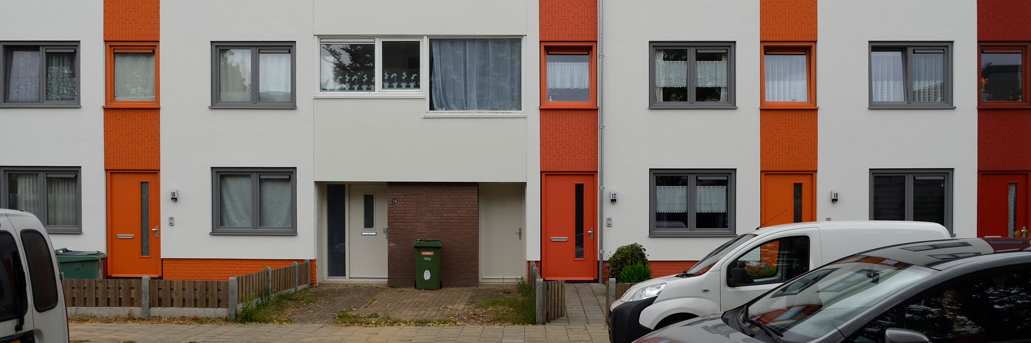 Woningen met witte gevels, grijze kozijnen, oranje accenten en voordeur.