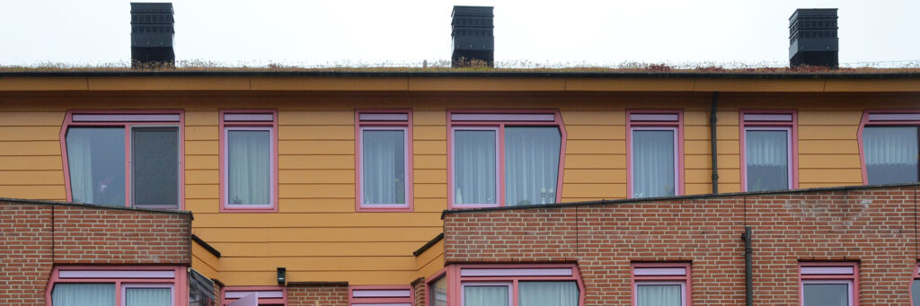 Woningen met een benedenverdieping van bakstenen met daarboven een verdieping met bruine planken en paarse kozijnen.