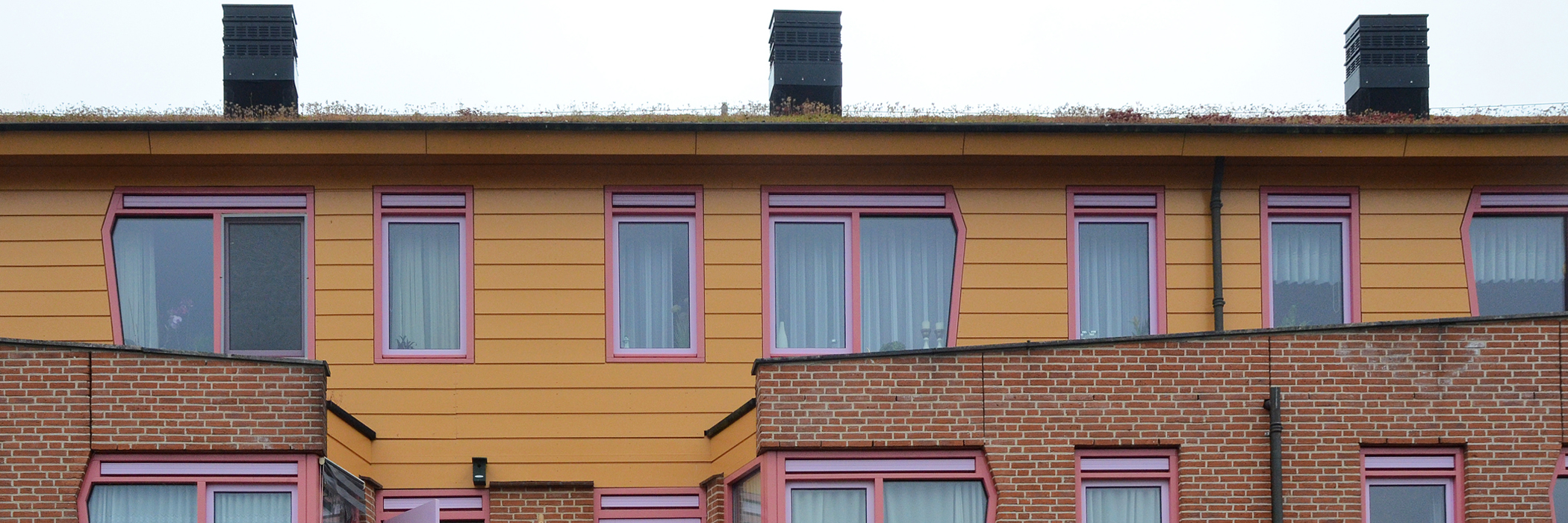 Woningen met een benedenverdieping van bakstenen met daarboven een verdieping met bruine planken en paarse kozijnen.