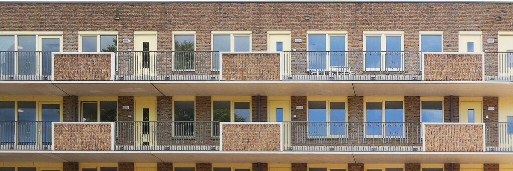 Appartementen van bakstenen, met een balkon, gele deuren en gele kozijnen.