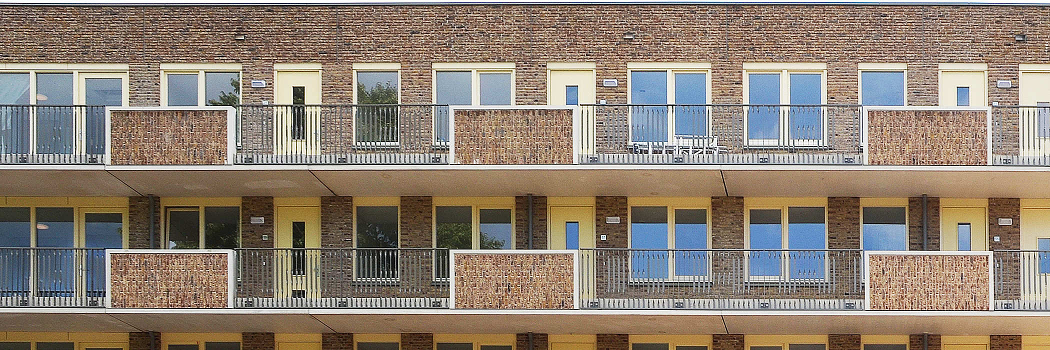 Appartementen van bakstenen, met een balkon, gele deuren en gele kozijnen.