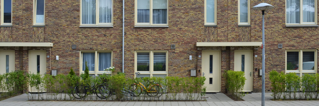 Woningen van bakstenen met een betegelde voortuin, gele deuren en gele kozijnen.