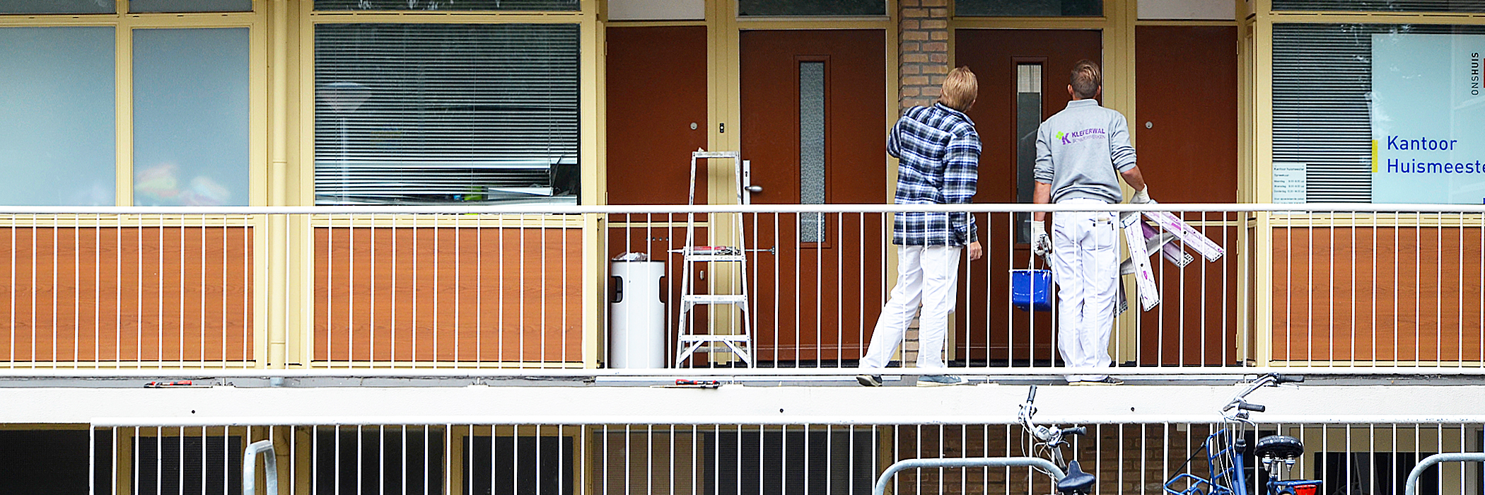 Appartementen met een rode voordeur, gele kozijnen en balken op de hoeken en een bruine plaat onder het raam.