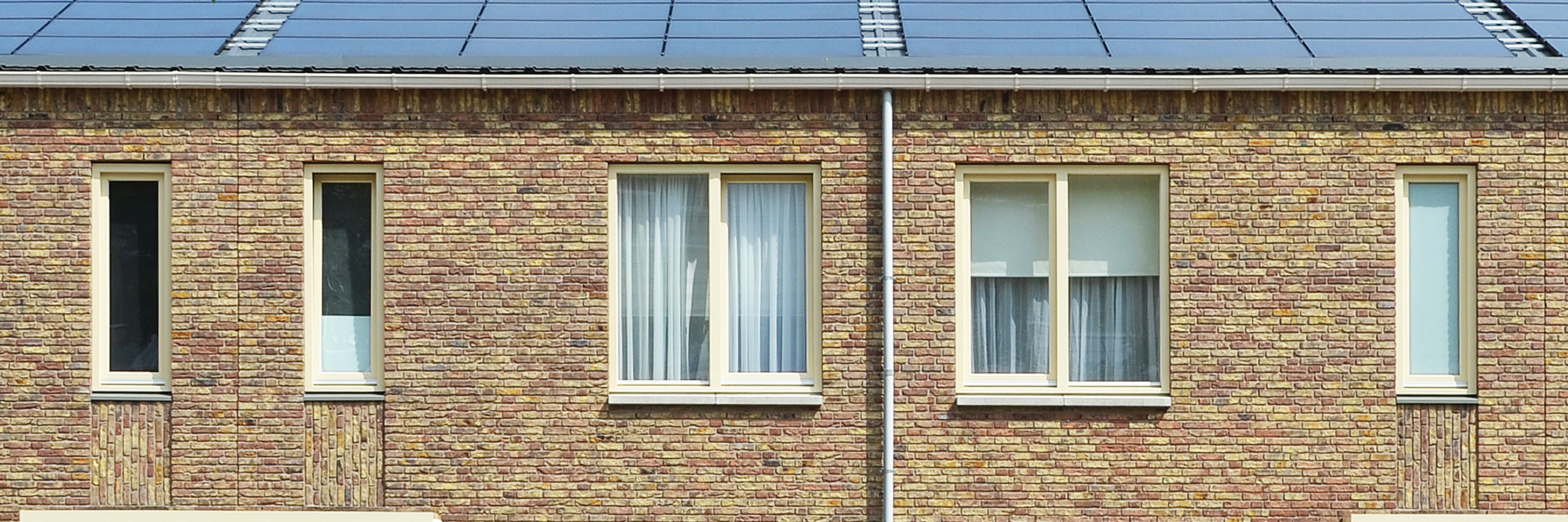Woningen van bakstenen met zonnepanelen op het dak en gele kozijnen langs de ramen.