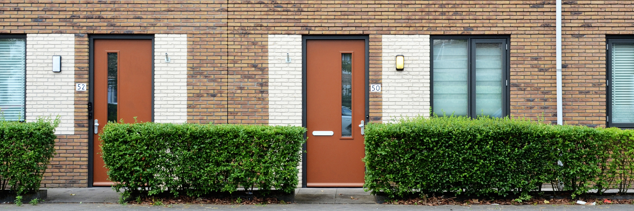 Woningen van bakstenen met naast het raam en de bruine voordeur een stuk met witte bakstenen.