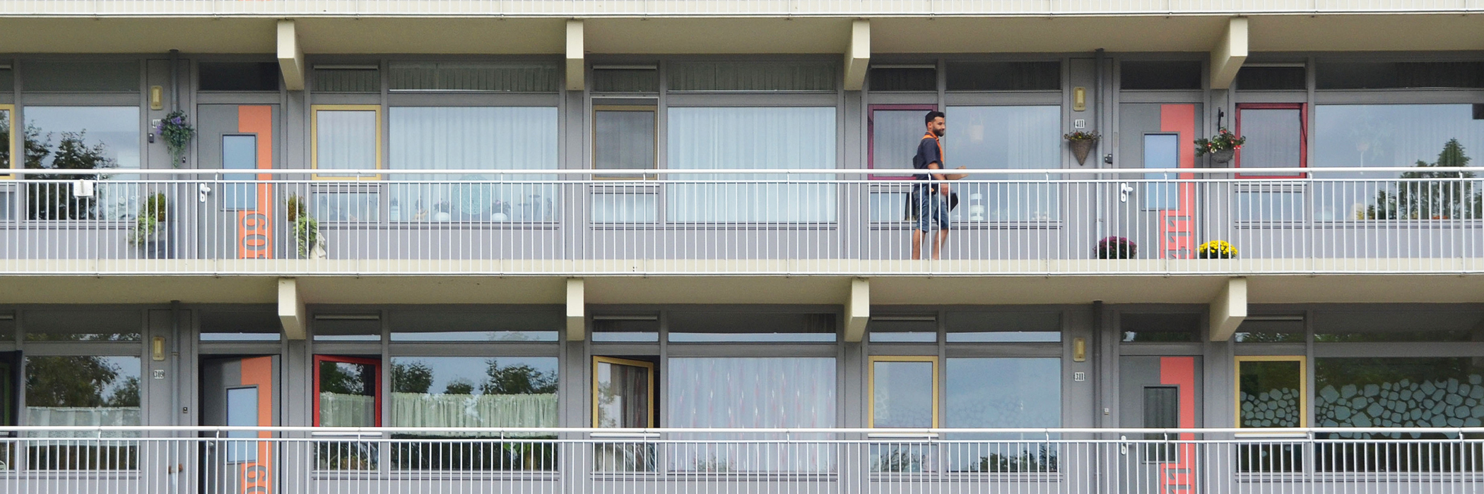 Appartementen met een grijze gevel, voordeur en kozijn, een wit balkon met een wit hekje.