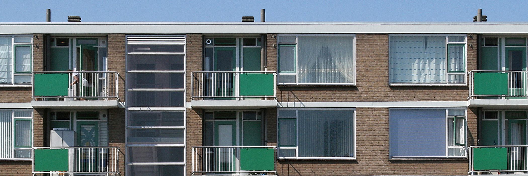 Appartementen van bakstenen met een groene deur, groene kozijnen en balkon met een wit hek en een groene plaat