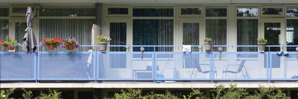 Appartementen met een witte deur, witte muur, witte kozijnen en balkon met een blauw hekje.