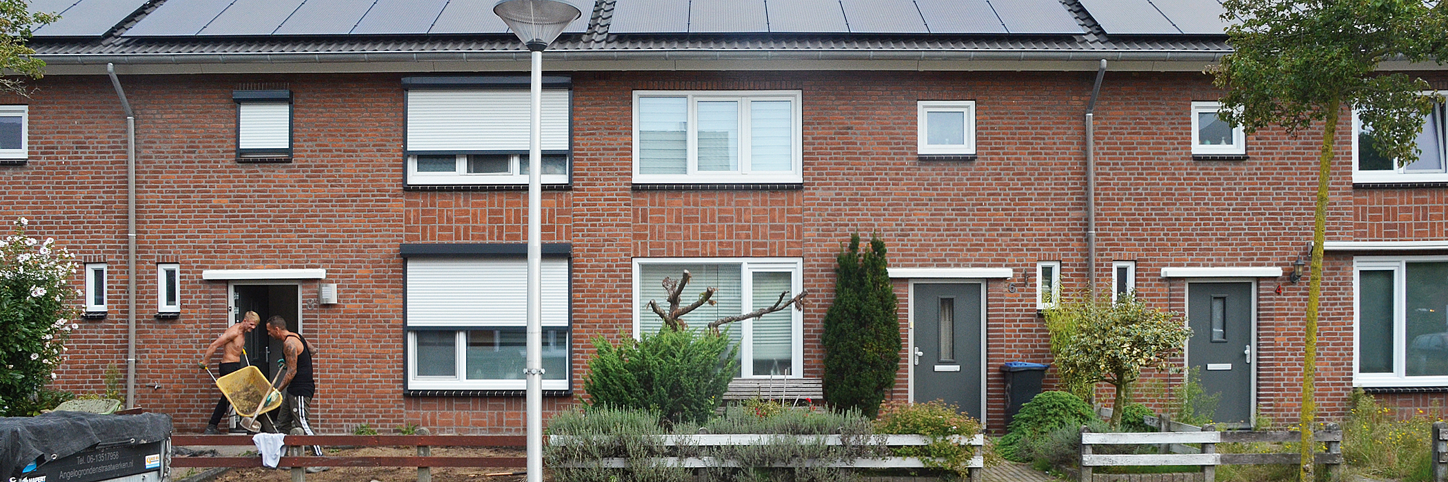 Woningen van bakstenen met zonnepanelen, grijze voordeur, witte kozijnen en donkere kozijnen.