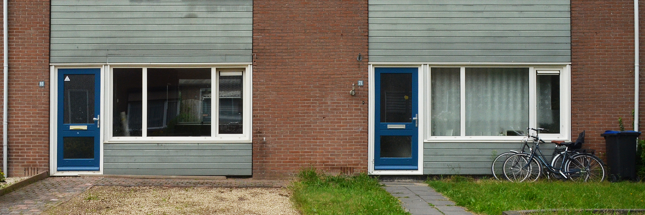 Woningen van bakstenen met een blauwe deur, witte kozijnen en horizontale houten balken.