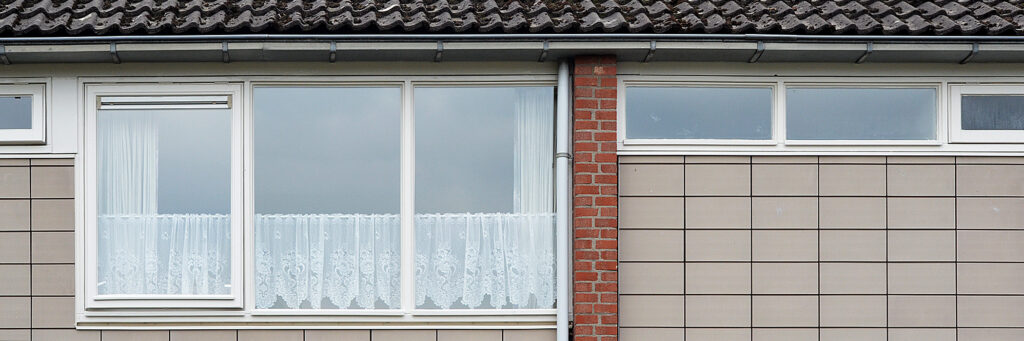 Woning met grijze tegels, witte kozijnen en een bakstenen verticale tussenlijn.