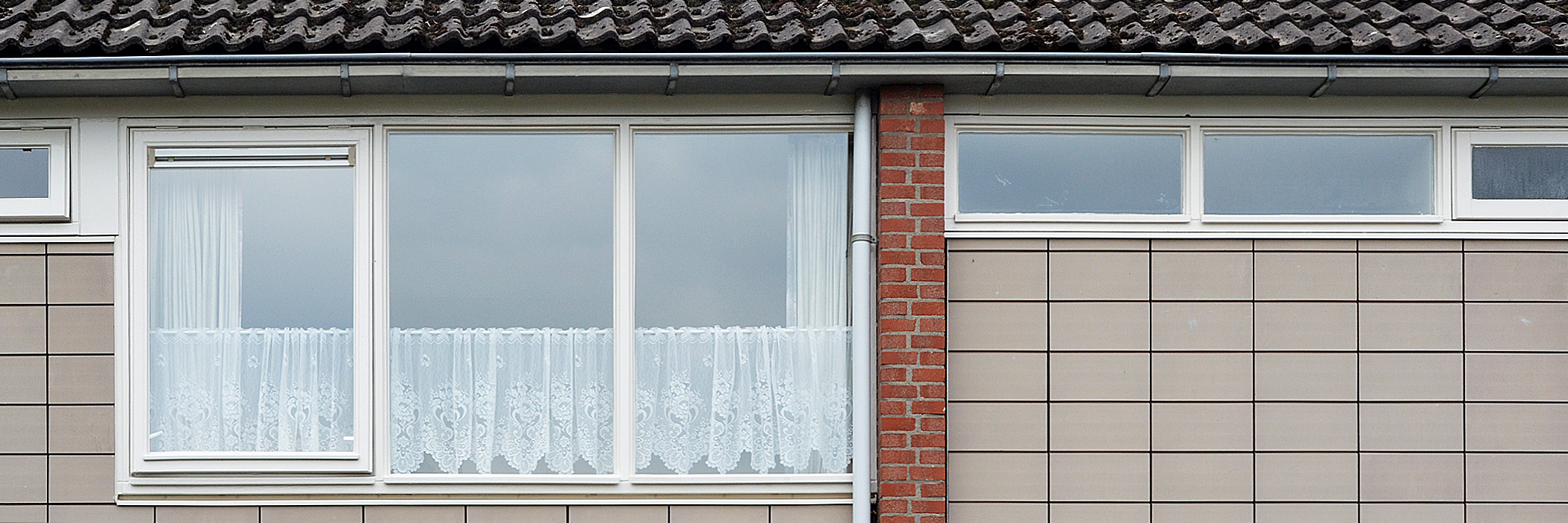 Woning met grijze tegels, witte kozijnen en een bakstenen verticale tussenlijn.