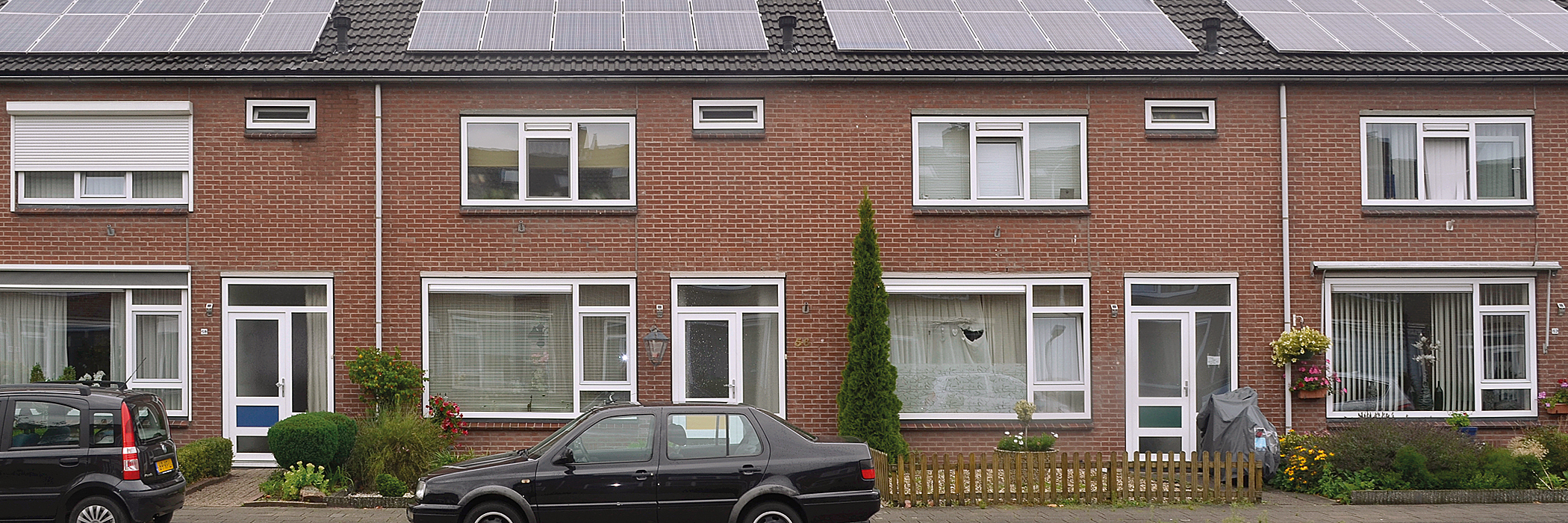 Woningen met zonnepanelen, witte voordeur, witte kozijnen en een voortuin.