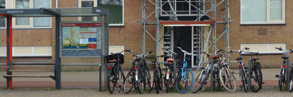 Appartementen van bakstenen voor een bushalte waar fietsen geparkeerd staan.