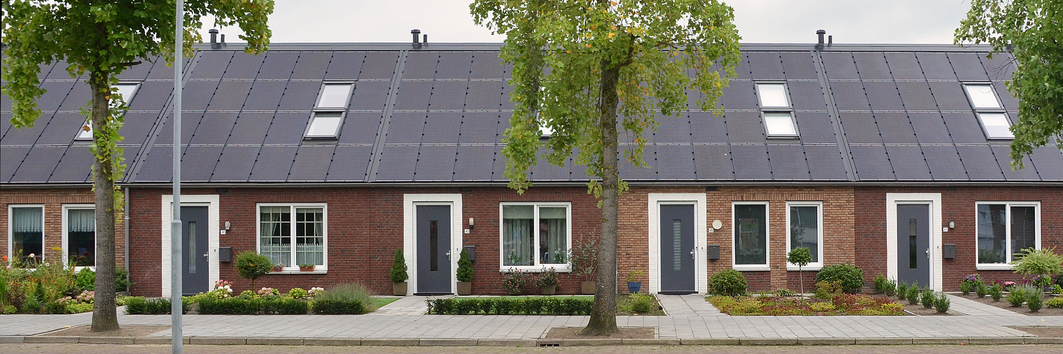Woningen van bakstenen met zonnepanelen, grijze deuren, witte kozijnen en groen voortuintje.
