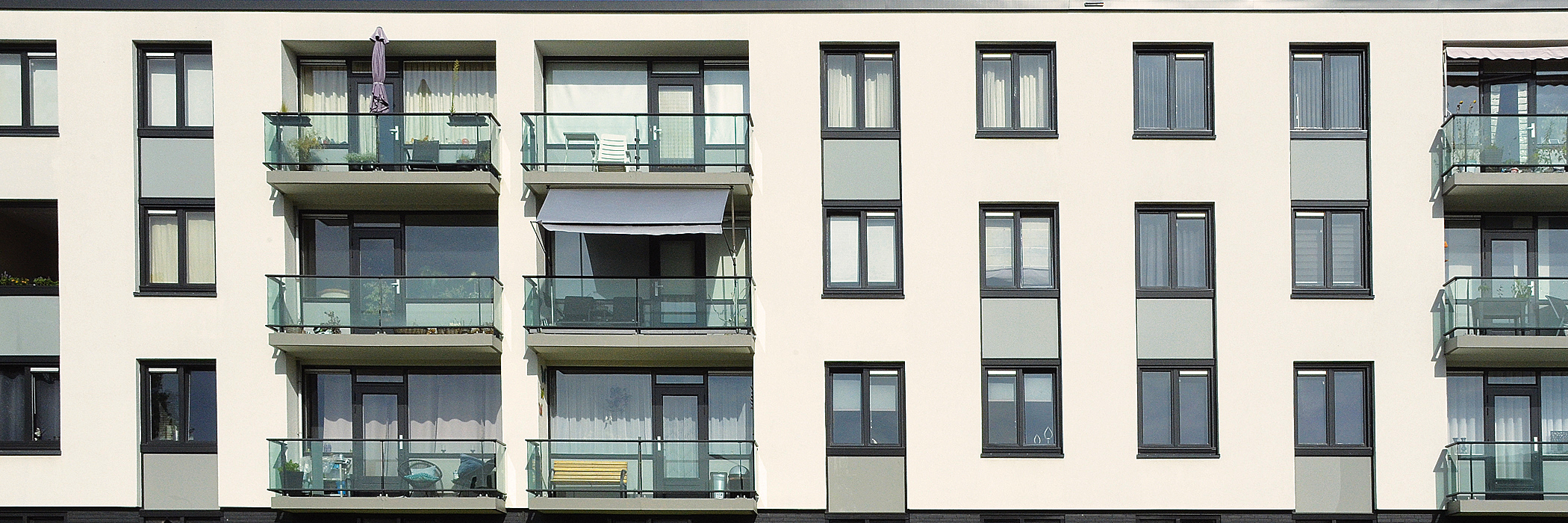 Appartementen met een witte gevel, zwarte kozijnen een balkon met een hekje van glas