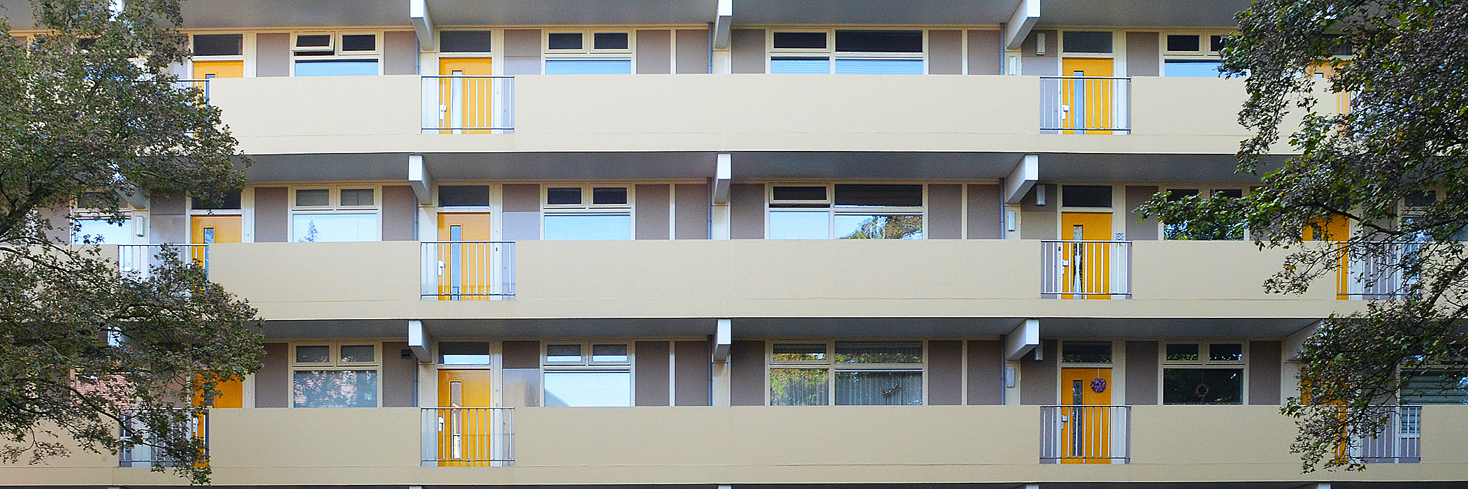 Appartementen met een donkergrijze gevel, witte kozijnen, oranje deur en een grijs balkon