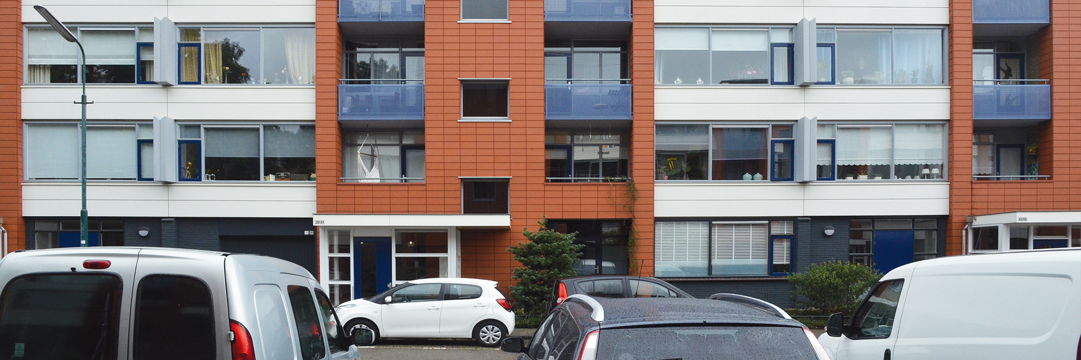 Appartementen met oranje tegels, verschillende kleuren kozijnen en een blauwe voordeur.