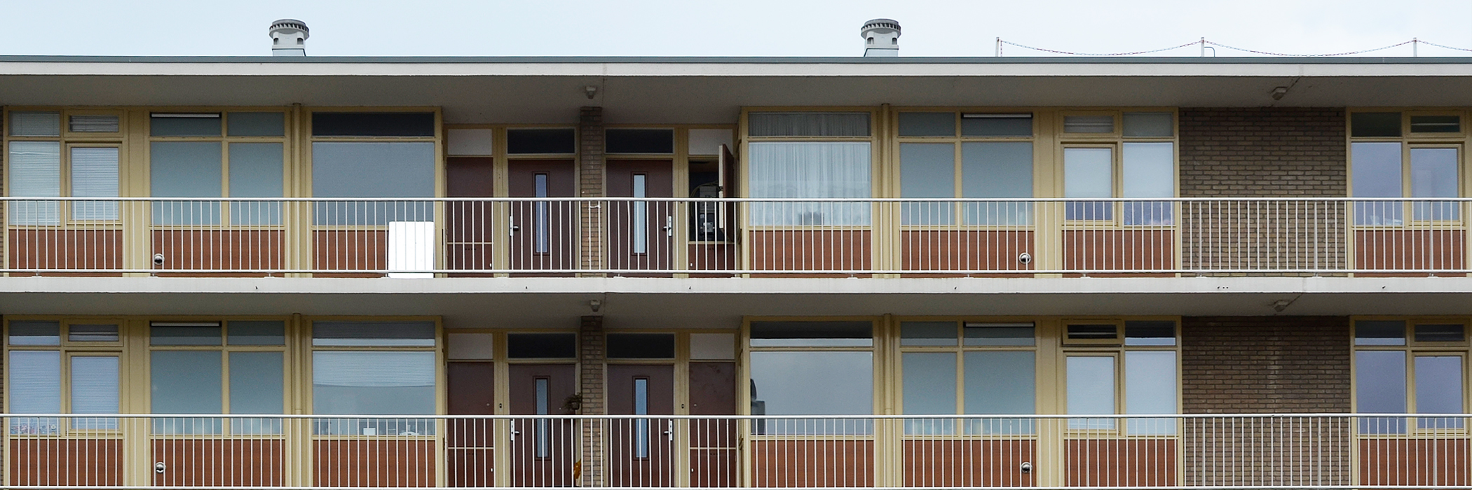 Appartementen van bakstenen met gele kozijnen, een balkon met wit hekje en bruine voordeur.