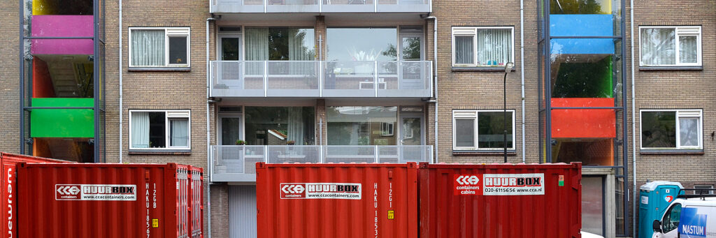Appartementen van bakstenen met balkon, witte kozijnen en een grijze deur.
