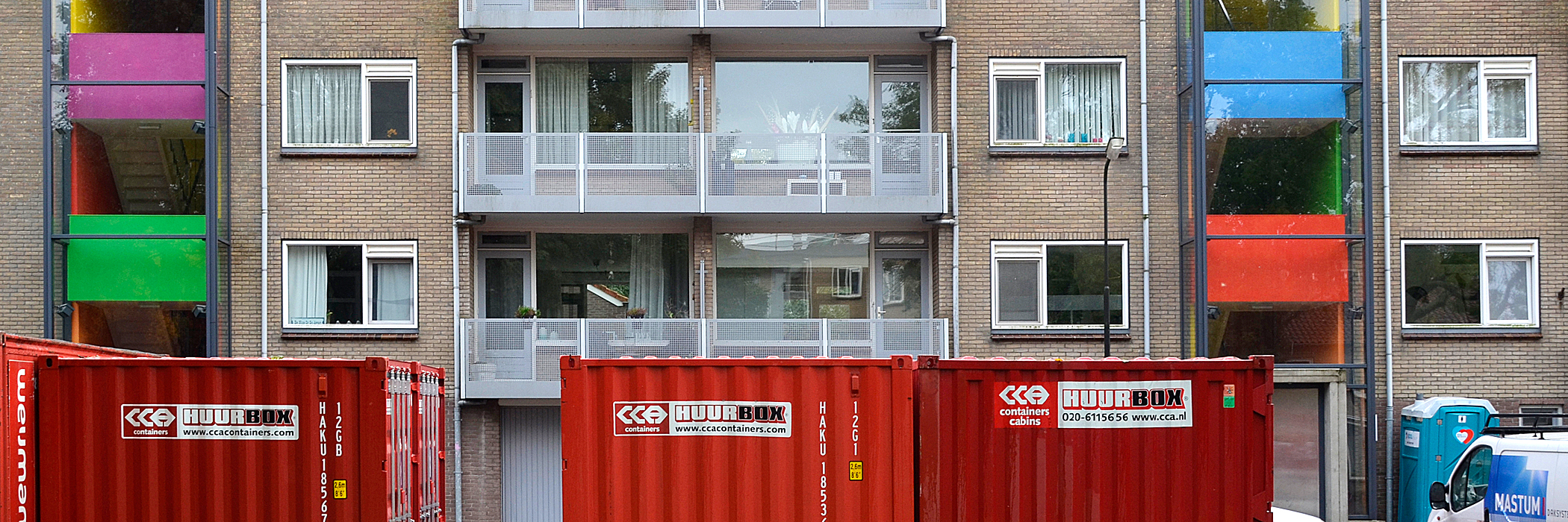 Appartementen van bakstenen met balkon, witte kozijnen en een grijze deur.