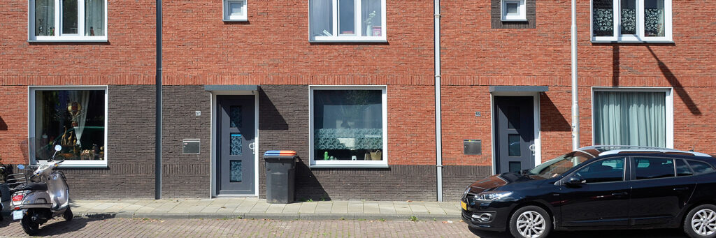 Woningen van donkere en oranje bakstenen, donkere voordeur en witte kozijnen.