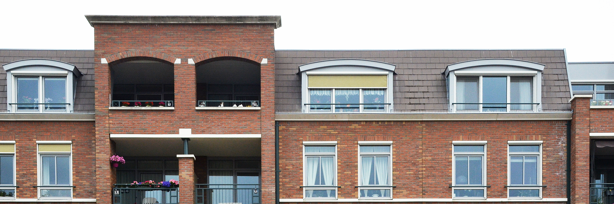 Appartementen met bruine bakstenen gevel, witte kozijnen, en grijze balustrade