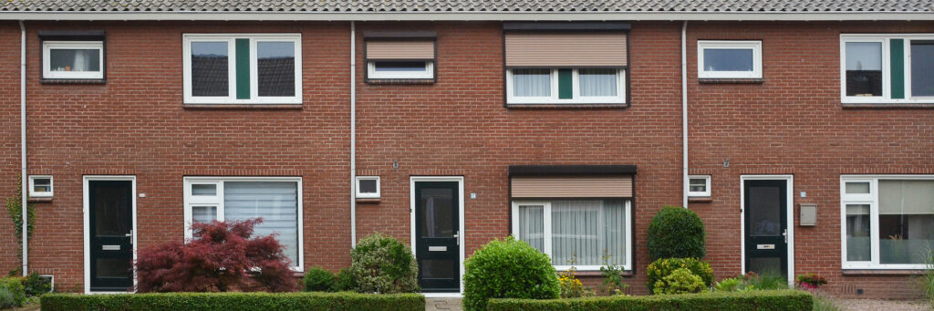 Woningen met bruine bakstenen gevel, witte kozijnen, donker groene deuren met bosjes voor de deur