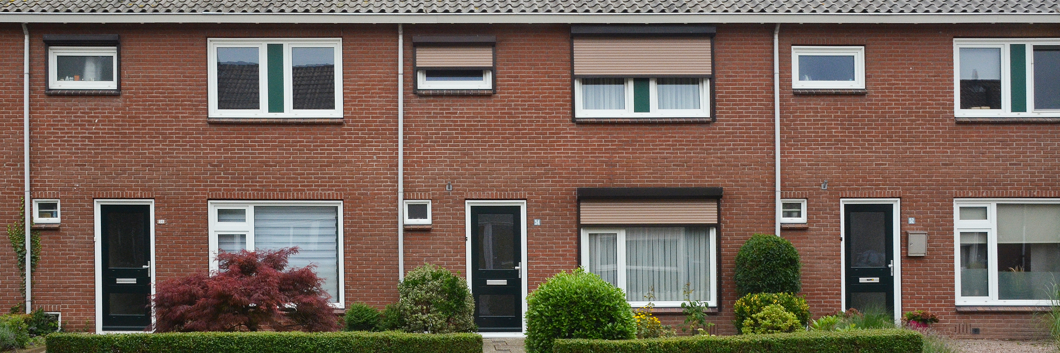 Woningen met bruine bakstenen gevel, witte kozijnen, donker groene deuren met bosjes voor de deur