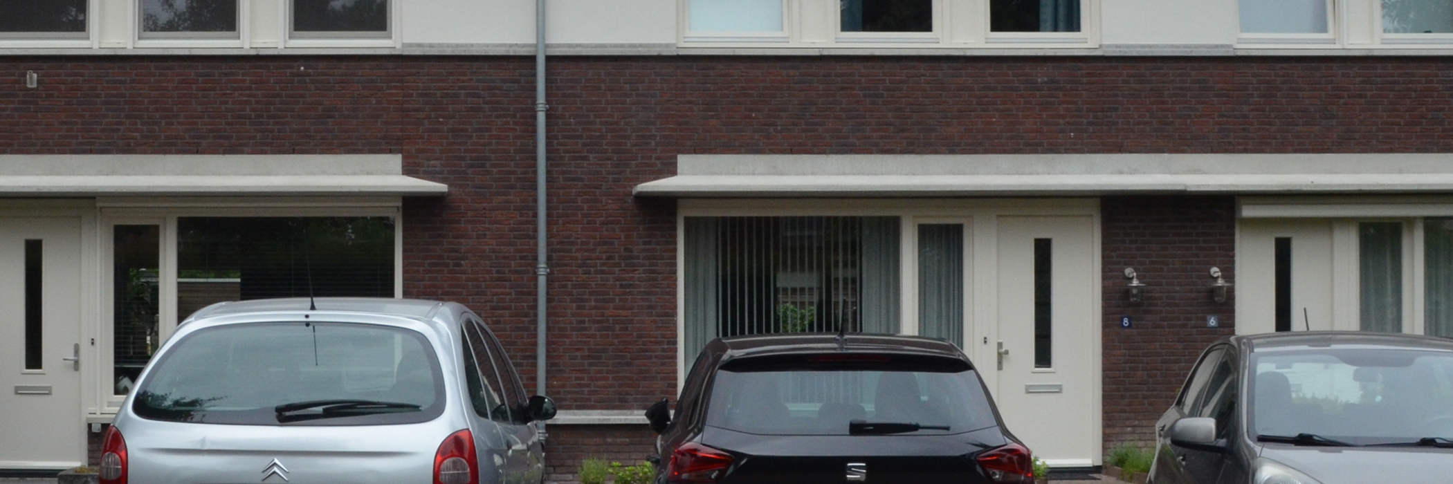 Woningen bruine bakstenen gevel, witte kozijnen en deuren met drie auto's voor de deur