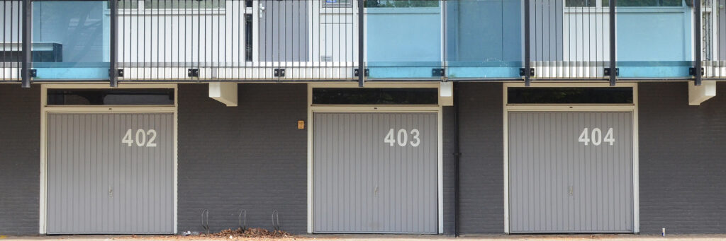 Appartementen met grijze bakstenen gevel, witte kozijnen met grijze deuren met op de begane grond drie garages met een grijze overhead deur