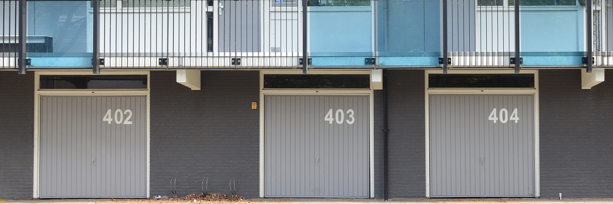 Appartementen met grijze bakstenen gevel, witte kozijnen met grijze deuren met op de begane grond drie garages met een grijze overhead deur