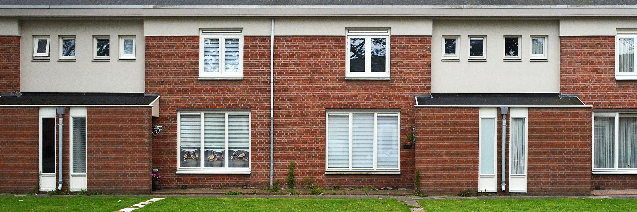 Woningen met rode bakstenen gevel, witte kozijnen en groen gras