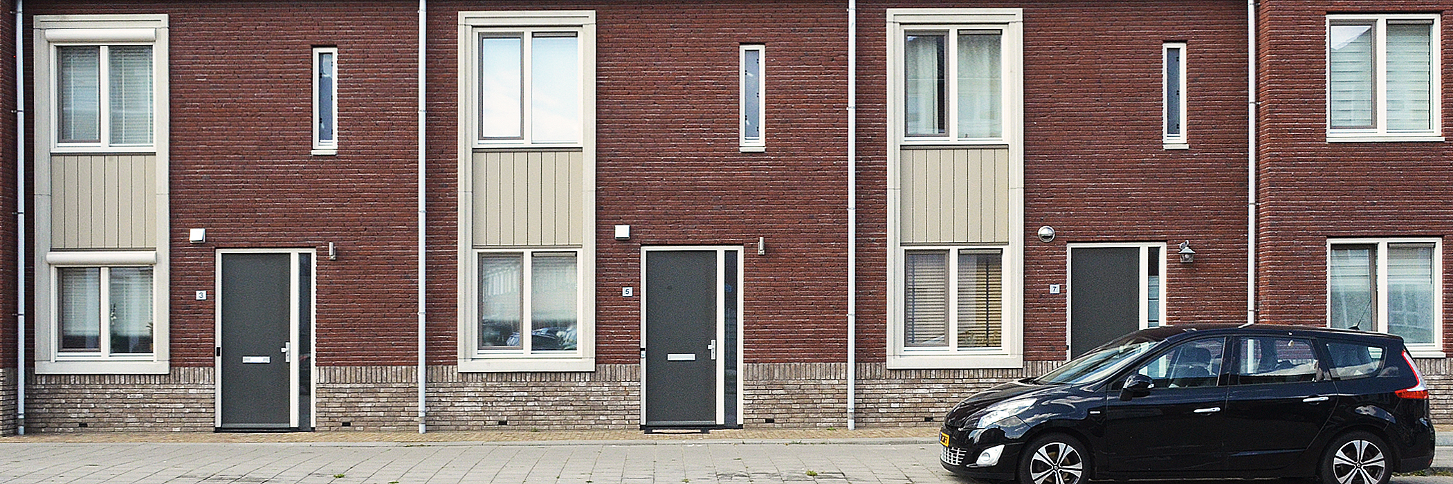 Woningen met rode bakstenen gevel, witte kozijnen, grijze deuren en een zwarte auto voor de deur