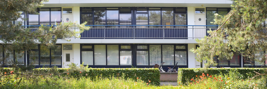 Appartementencomplex met donkerblauwe kozijnen, witte deuren en struiken voor het gebouw