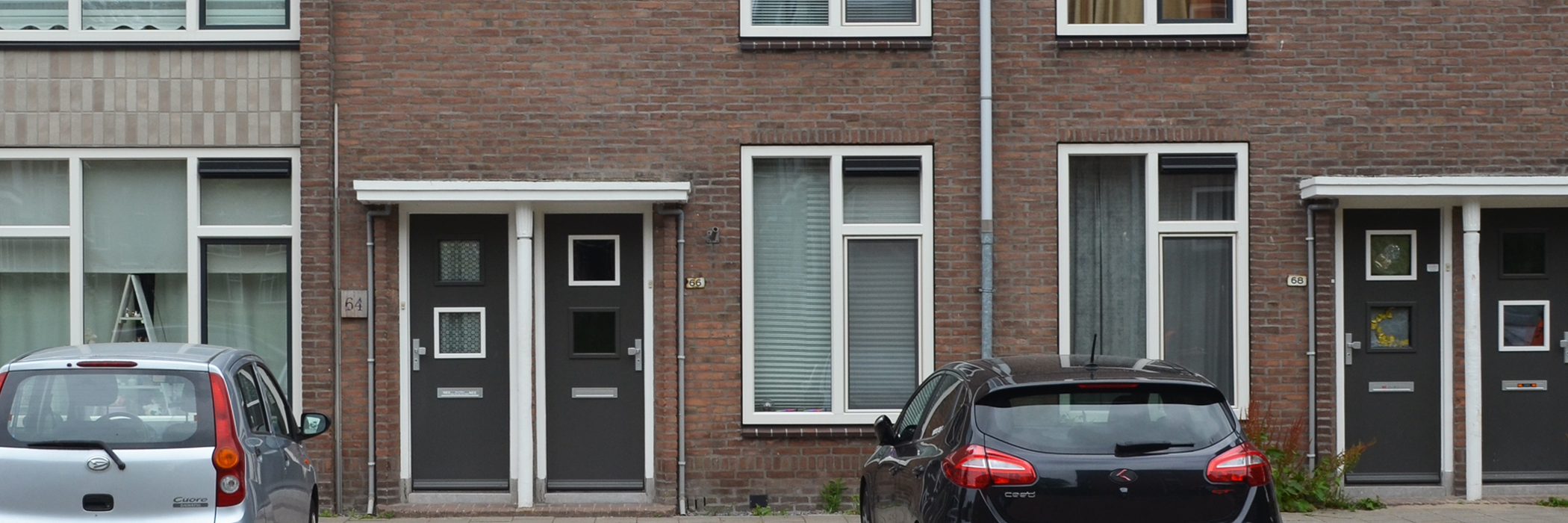Entree van vier woningen met witte kozijnen en grijze deuren. voor de woningen zijn parkeerplaatsen met auto's