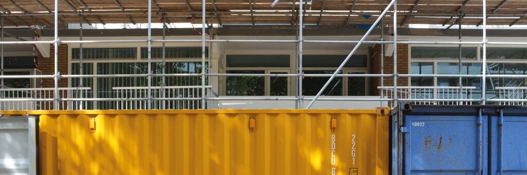 Appartementencomplex waar een stijger voorstaat en een gele en blauwe afvalcontainer.