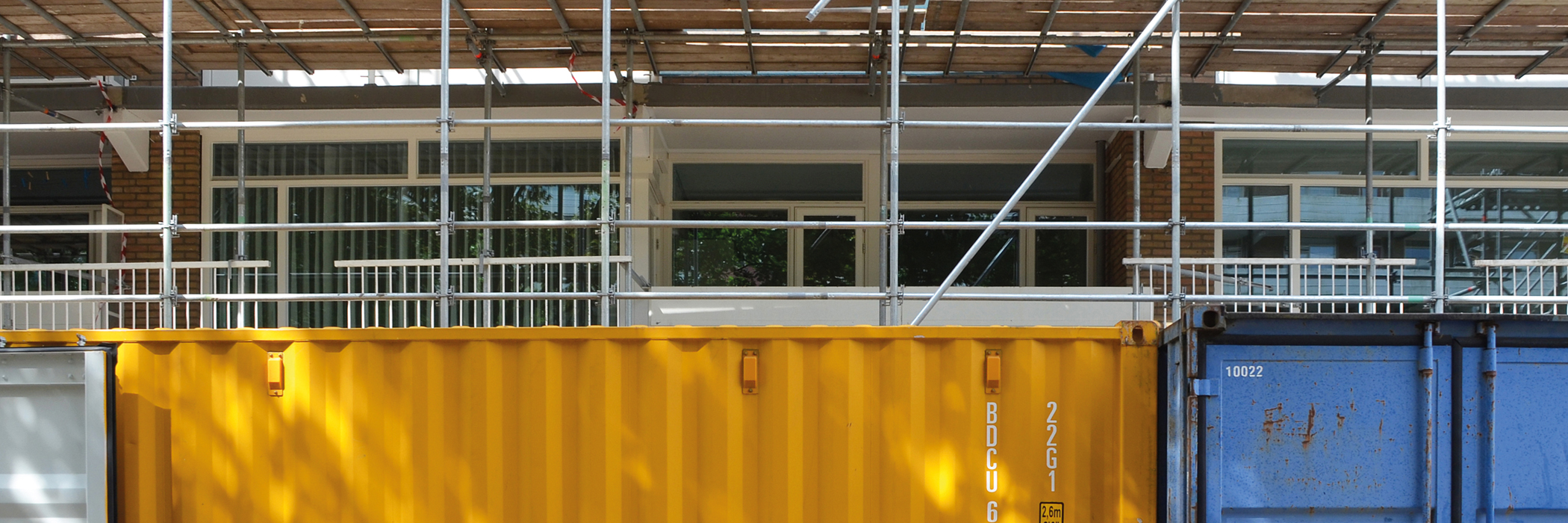 Appartementencomplex waar een stijger voorstaat en een gele en blauwe afvalcontainer.