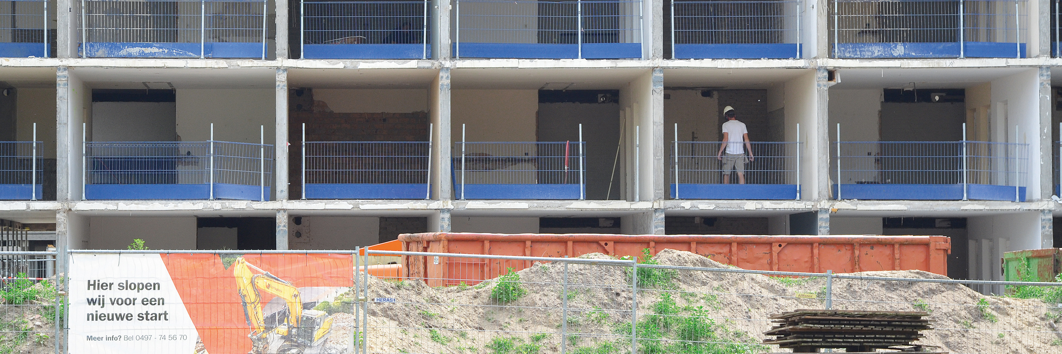 Een flatgebouw die gerenoveerd word, voor het flatgebouw staat een oranje afvalcontainer.